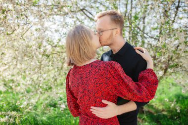 Güneşli bir bahar gününde çiçek açan bir ağacın arka planında güzel bir çift öpücüğü ve kucaklaşması.