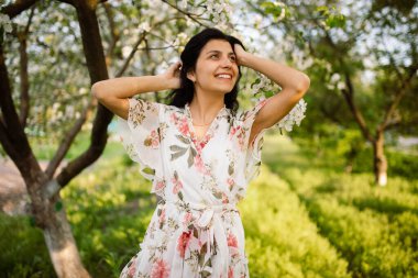Güzel bir bahar gününde çiçek açan bir bahçede poz veren esmer bir kadının yakın çekimi. Mutluluk, rahatlama ve aşk kavramı