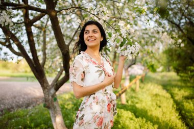 Mutlu, güzel esmer, dişleriyle gülümseyen ve baharın sıcacık bir gününde çiçek açan bir bahçe parkında gülen.
