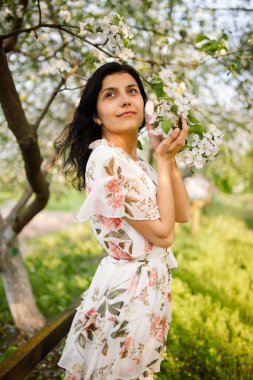 Çekici, güzel bir kadın, güzel bir bahar gününde, çiçek açan bir bahar bahçesinde beyaz çiçeklerin arka planına yaslanır.