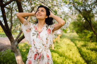 Mutlu, güzel esmer, dişleriyle gülümseyen ve baharın sıcacık bir gününde çiçek açan bir bahçe parkında gülen.