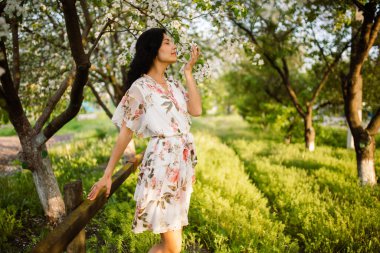 Genç ve güzel bir kadın bahar bahçesinde çiçek açan ağaçların kokusundan zevk alır. Kırsal alan. İlkbahar