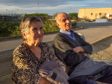 Yaşlı bir çift bankta oturmuş birilerine gülümsüyor. Kopyalamak için boşluk