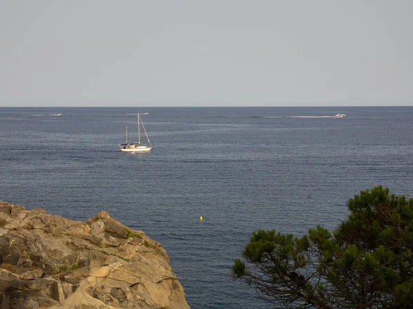 Small sailboat seen from the rocks, sailing on a silver sea on a sunny day. Vacation concept.