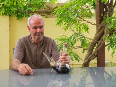 Yaşlı bir adam elinde bir bardak kırmızı şarapla masada oturuyor. Şarap için cam sürahi tipik İspanya şarabı..