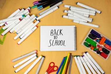 Many different office supplies. School markers, pens and plasticine. Inscription on notebook back to school.