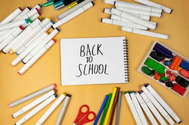 Many different office supplies. School markers, pens and plasticine. Inscription on notebook back to school.