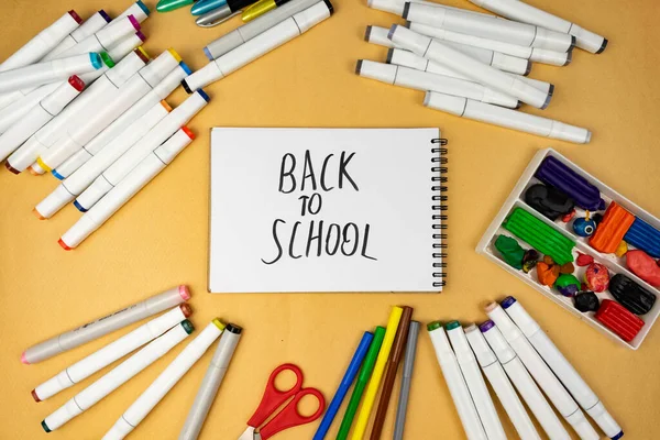 Many different office supplies. School markers, pens and plasticine. Inscription on notebook back to school.