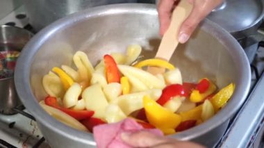 Dişi aşçı büyük bir tatlı biber pişirir ve ahşap bir spatulayla karıştırır. Evde lezzetli yemekler pişirmek.