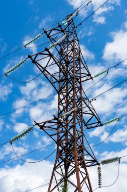 Beyaz bulutlu mavi gökyüzünün arka planında yüksek voltajlı bir elektrik hattı..
