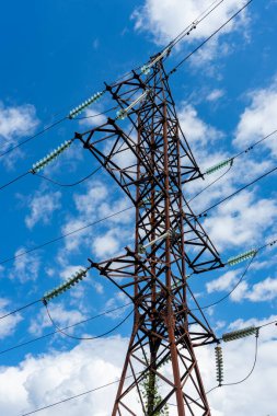 Beyaz bulutlu mavi gökyüzünün arka planında yüksek voltajlı bir elektrik hattı..