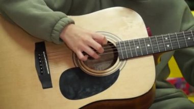Akustik gitarın tellerini bir genç seçiyor. Gitar çalmayı öğreniyorum. Gitarı yakın plan çalıyorum.