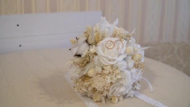 花嫁の美しい花束 白いテーブルの上に結婚指輪と花嫁の花束 カメラにぶつかった スタビライザーを使って — ストック動画