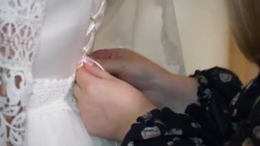 Bir nedime gelinliğindeki gelinlikleri kontrol eder. Gelinlik giyiyor.