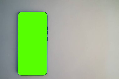 Canlı yeşil ekranlı akıllı bir telefon açık renkli bir yüzeye oturur. Uygulamaların yokluğu, aygıtın kolay içerik oluşturulmasına veya düzenlenmesine olanak tanır. Dijital projeler için ideal.