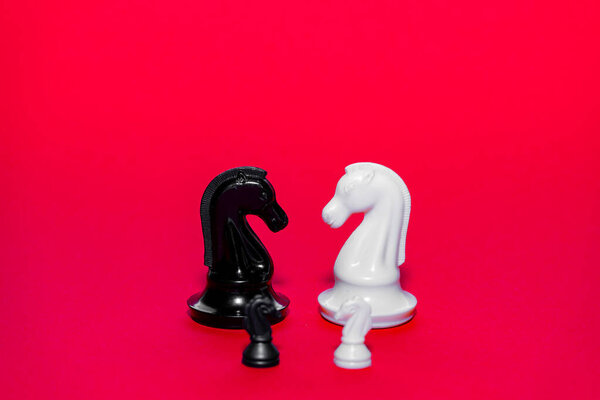 Two chess pieces, a black knight and a white knight, are prominently displayed on a striking red background, highlighting the contrast between the colors in a playful board game setting.
