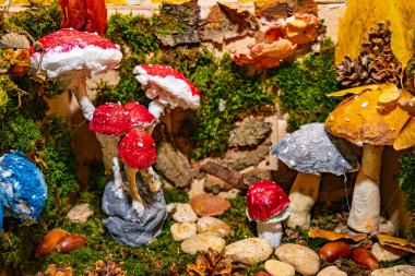 Kırmızı ve gri renkli el yapımı mantarlar yosun ve taşların arasında duruyor. Sonbahar yaprakları ve çam kozalakları çevresindeki doğal dekor ve sanat eserlerini geliştirir..