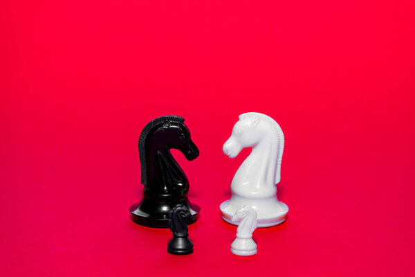 Two distinct chess pieces stand prominently against a bright red backdrop, emphasizing the classic battle between black and white. The moment captures the strategic essence of chess.