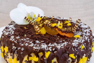 Güzel hazırlanmış bir çikolatalı pasta renkli meyveler, çıtır çıtır şeritler ve narin beyaz orkidelerle bezenmiş zengin bir krema içerir. Bu da onu kutlamalar için mükemmel bir tatlı yapar..