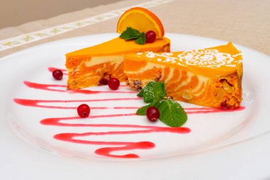 Çok güzel hazırlanmış bir tatlı, turuncu kremalı pasta dilimleri ve canlı bir girdap tasarımı. Taze nane yaprakları, kızılcıklar ve bir tutam meyve sosuyla süslenmiş, cezbedici görünüyor..