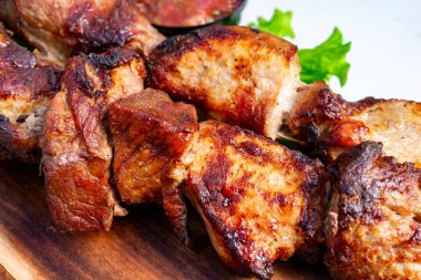 Tahta bir tahtanın üzerinde taze yeşilliklerle sıralanmış yumuşak et parçaları. Yemeklere eşlik eden küçük bir kase sos, lezzetli tatların her türlü toplanma için mükemmel olduğunu vurgular..