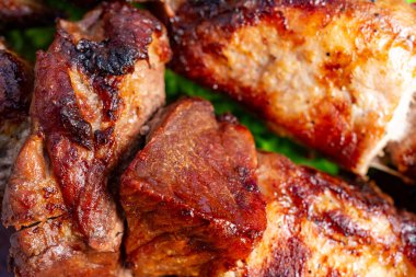 Lezzetli ızgara et parçaları, zengin ve kömürleşmiş görünüşlerini gösteren bir tabakta yakın bir şekilde sıralanır. Unutulmaz bir açık hava barbekü deneyimini çağrıştıran bir koku..