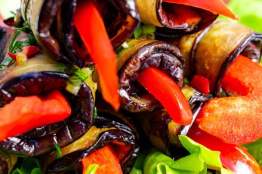 Canlı dolma biberlerle dolu rulo patlıcan katmanları taze yeşilliklerin üzerinde ustalıkla düzenlenmiştir. Bu renkli yemek, dokuların ve tatların hoş bir karışımını sergiliyor..