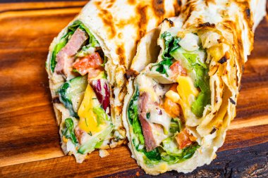 Canlı bir paket ambalajı taze marul, domates, dilimlenmiş et ve peynir katmanları mükemmelce kızartılmış ve hızlı bir yemek için ideal, kırsal ahşap bir tahtanın üzerinde servis edilir..