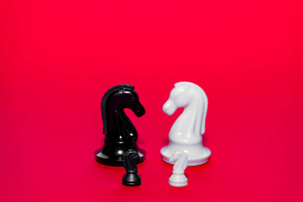 Two chess pieces, one black and one white, stand facing each other on a vivid red background. Each piece is intricately designed, poised for an exciting match between players.