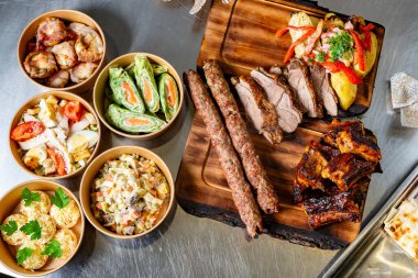 Pirzola ve şişler de dahil olmak üzere canlı bir ızgara et karışımı, taze salatalar ve yanlarla eşleştirilmiş, toplanma ve kutlamalar için mükemmel bir ziyafet sunuyor..