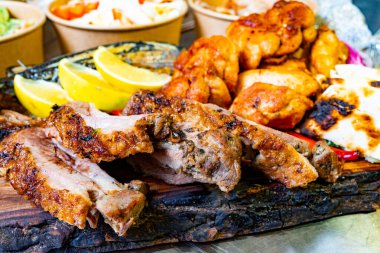 Güneşli bir öğleden sonra bir açık hava toplantısında ızgara et, limon ve canlı mezeler ahşap bir tabakta sergileniyor ve konukları ziyafetin tadını çıkarmaya davet ediyor..