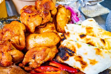 Yumuşak ızgara tavuk parçaları, canlı bir açık hava buluşmasında sıcak yassı ekmek ve renkli sebzelerin yanında, ağız sulandırıcı bir lezzet gösterisi oluşturur..