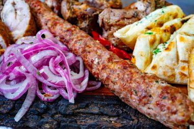 Lezzetli bir ızgara et çeşidi sosis ve tavuk, yanında sıcak ekmek ve canlı kırmızı soğan, tadını çıkarmaya hazır bir ziyafeti vurguluyor..