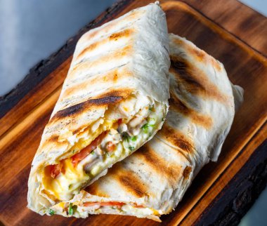 Çırpılmış yumurta, sebze ve peynirle dolu taze ızgara kahvaltı burritosu ahşap bir tabakta sunulur. Altın sarısı, ızgara, dışa dönük şehvet uyandırır..