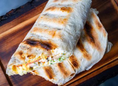 Renkli sebze ve peynirle dolu iki ızgara burrito kırsal bir ahşap tahtada sergileniyor. Doku davetkar, nefis yanmış dış görünüşü sergiliyor..