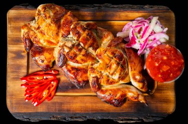 Sulu ızgara tavuk, taze dilimlenmiş soğanlar, baharatlı biberler ve daldırmak için ideal bir sos eşliğinde sade ahşap bir tabakta sunuluyor..