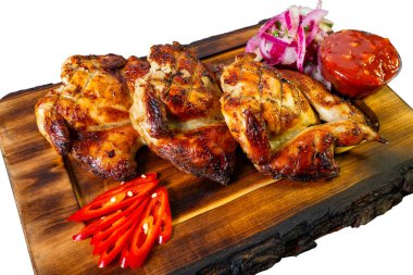 Juicy grilled chicken pieces are arranged on a rustic wooden platter, accompanied by fresh red onion, spicy sauce, and sliced chili peppers, creating an inviting meal setting. clipart