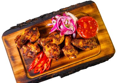 Sulu ızgara tavuk kanatları ahşap bir tepside sunulur. Renkli kırmızı soğanlar, taze biberler ve keskin soslar yemeğe eşlik ederek lezzetli ve davetkar bir yemek hazırlıyorlar..