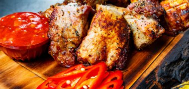 Baharatlı ızgara et şişleri ahşap bir tahtanın üzerinde keskin bir sos ve canlı kırmızı biber dilimleriyle kaplıdır. Tabakta zengin dokular ve iştah açıcı renkler sergileniyor.