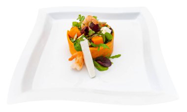 Parlak renkli deniz ürünleri salatası beyaz bir tabakta karides, yeşillik ve süslemeler içerir. Modern bir yemek ortamında hafif bir yemek ya da aperatif için ideal..