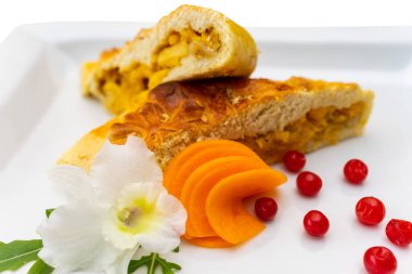 Lezzetli bir dilim lezzetli turta, taze meyve dilimleri, parlak kırmızı böğürtlenler ve zarif bir çiçekle süslenmiş beyaz bir tabakta servis edilir..