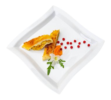 Lezzetli hamur işi, yanında havuç bukleleri ve kırmızı böğürtlen gibi renkli süslemelerle beyaz bir tabakta zarif bir şekilde oturur. Sunum yemeğin cazibesini vurguluyor.