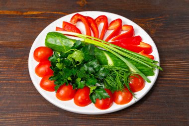 Kırmızı dolma biber, kiraz domatesleri, yeşil soğanlar ve yapraklı yeşilliklerin yer aldığı canlı bir sebze tabağı üzerinde sergilenmektedir. Bu sağlıklı düzenleme doğal ürünlerin güzelliğini vurgular..