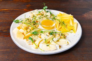 Çok güzel düzenlenmiş bir peynir tabağında çeşitli kremalı peynirler, taze mango dilimleri, bademler ve küçük bir kase bal bulunur..