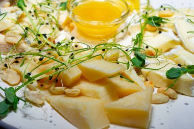 Çeşitli peynir çeşitleri bir tabakta sanatsal olarak düzenlenir. Peynirlere taze lahanalar ve küçük bir kase altın bal eşlik eder. Görsel cazibeyi arttırır..