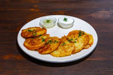 Otlarla süslenmiş tuzlu gözlemeler iki küçük kase kremalı sosla birlikte beyaz bir tabakta otururlar. Ahşap masa sıcak, kırsal bir dokunuş ekliyor..