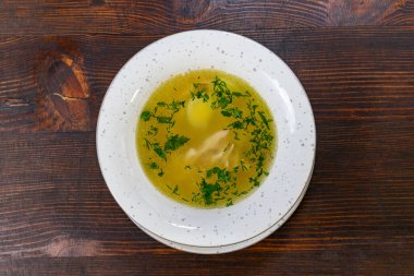 Bir kase haşlanmış tavuk çorbası. İçi taze tavuk parçaları ve taze otlarla dolu. Enerjik et suyu kırsal ahşap masada parlıyor..