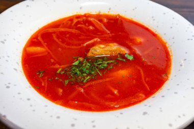 Yumuşak sebzelerle dolu canlı kırmızı bir borç ve et beyaz bir kasede oturur. Taze bitkiler üzerine serpilmiş, cezbedici görünümünü arttırıyor. Sıcak bir yemek için mükemmel.