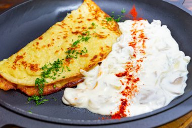 Yumurtadan yapılan lezzetli bir omlet, yanında baharatlarla süslenmiş kremalı yoğurt tabağında servis edilir. Bu yemek canlı renkler ve zengin dokular sergiliyor.