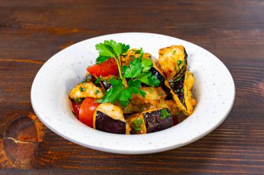 Taze hazırlanmış patlıcan ve domatesli sebze tabağı, otlarla süslenmiş, ahşap bir masada beyaz bir kasede servis ediliyor. Sağlıklı lokantalar için cazip bir yemek..